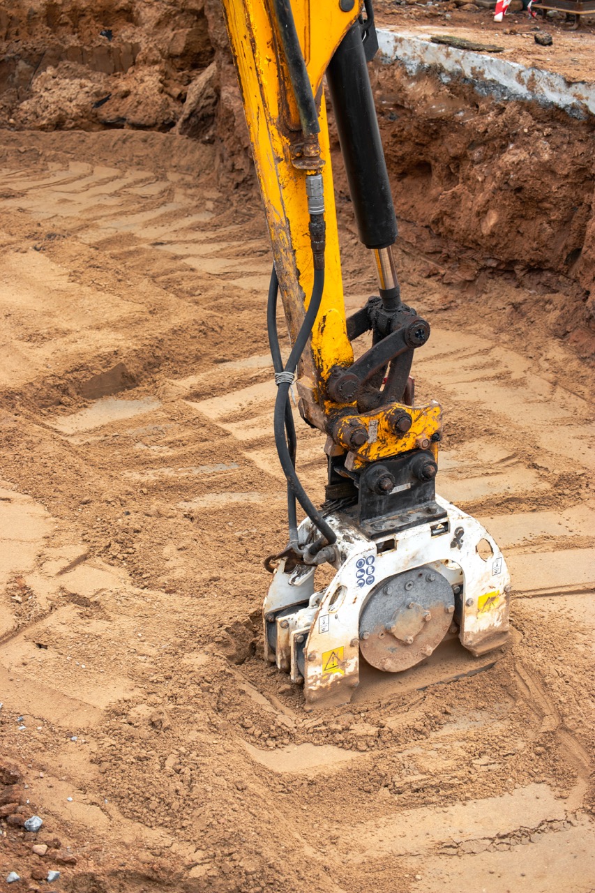 Excavator bucket dropping dirt into an open trench.
