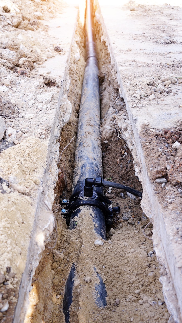 Excavator bucket dropping dirt into an open trench.